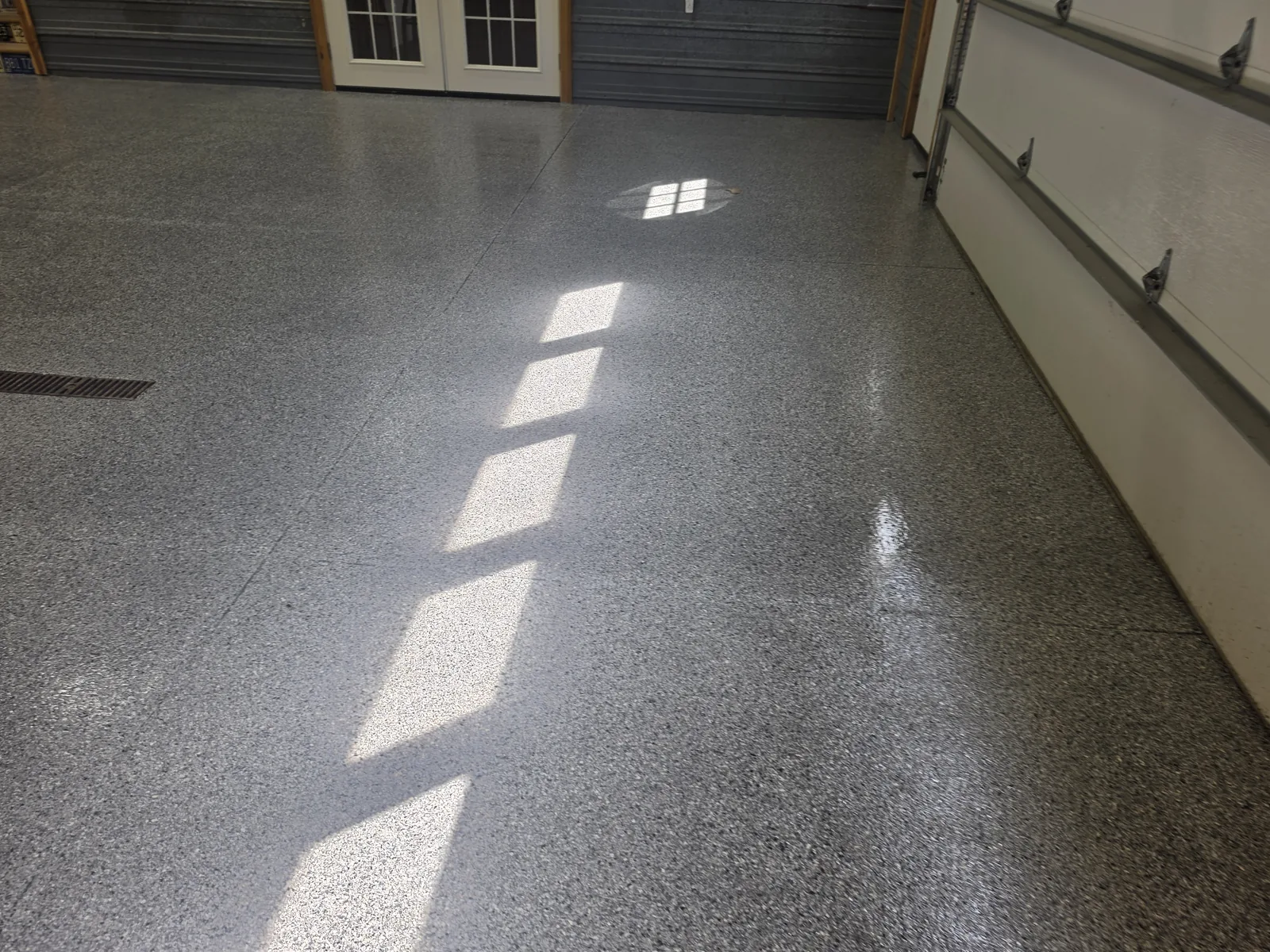 Sunlight across a glossy gray full-flake garage floor coating next to the garage door