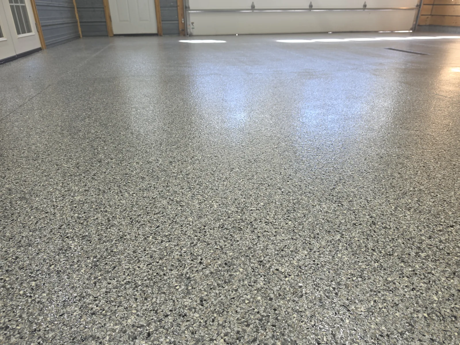 Glossy full-flake polyaspartic garage floor, wide view toward the overhead doors, West Michigan
