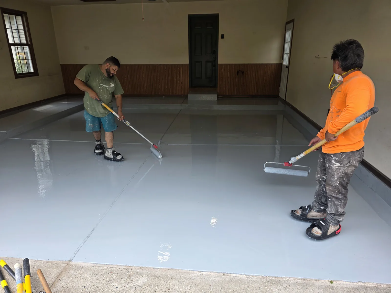 Armorforge crew rolling on the polyaspartic base coat in spiked shoes during a Grand Rapids garage floor installation